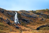 A peaceful waterfall cascading over rocky cliffs surrounded by autumn foliage.