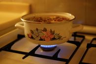 A floral design enamel pot on a gas stove with simmering soup, creating a warm kitchen ambiance.