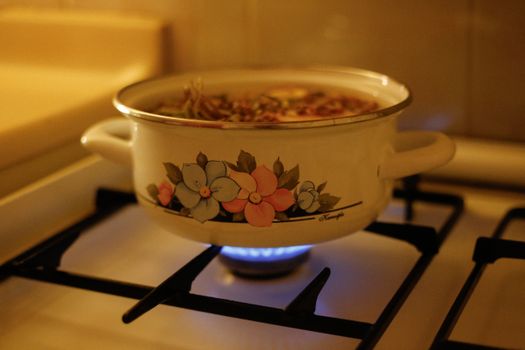 A floral design enamel pot on a gas stove with simmering soup, creating a warm kitchen ambiance.