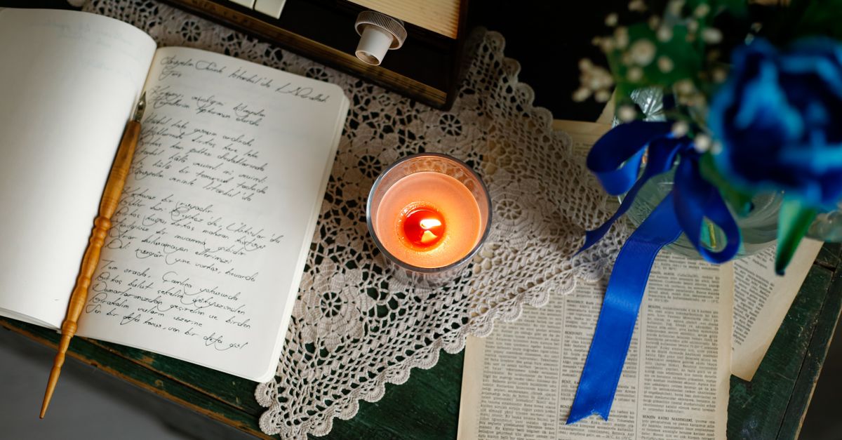 person writing in a journal by candlelight, phone turned face down on a table