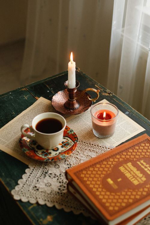 Free Warm cozy setup with a coffee cup, lit candles, and a book in a serene ambiance. Stock Photo