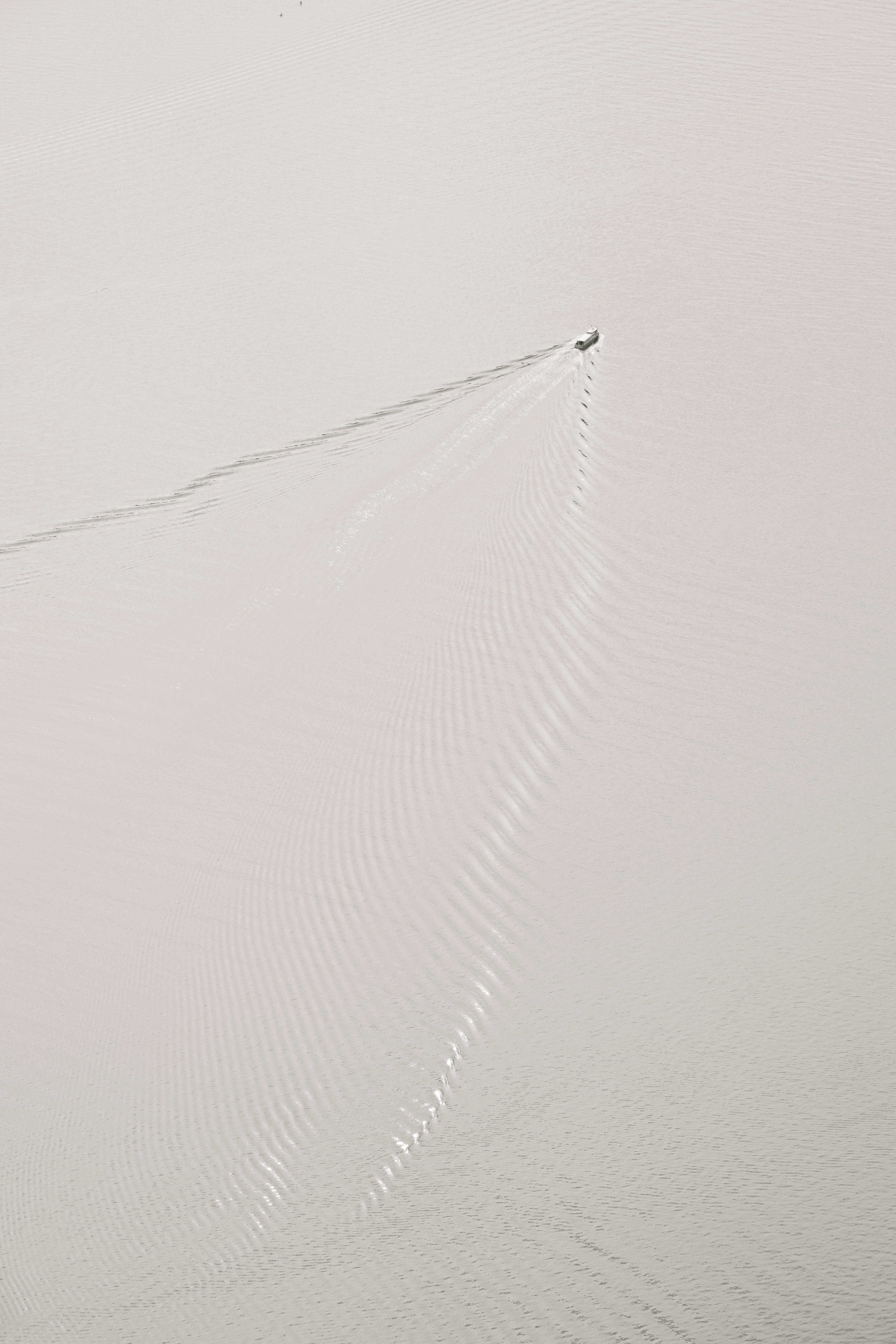 Gratis Vista aerea di una barca che crea increspature sulla superficie calma dell'acqua, minimalista e serena. Foto a disposizione