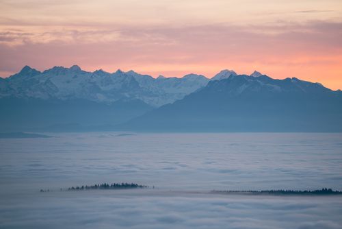 Free A breathtaking view of snow-capped mountains above a sea of clouds during sunrise. Stock Photo
