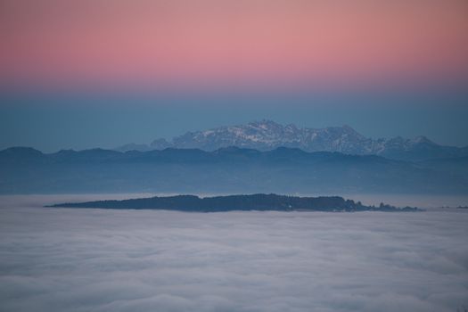 Serene mountain landscape at sunset with a blanket of clouds and pastel skies creating a calm, atmospheric view.
