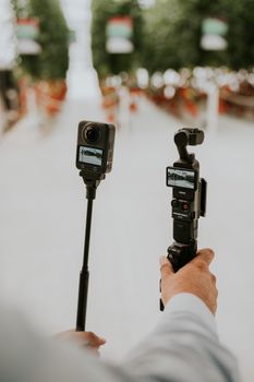 Hands holding advanced cameras capturing an outdoor scene, showcasing modern photography tools.