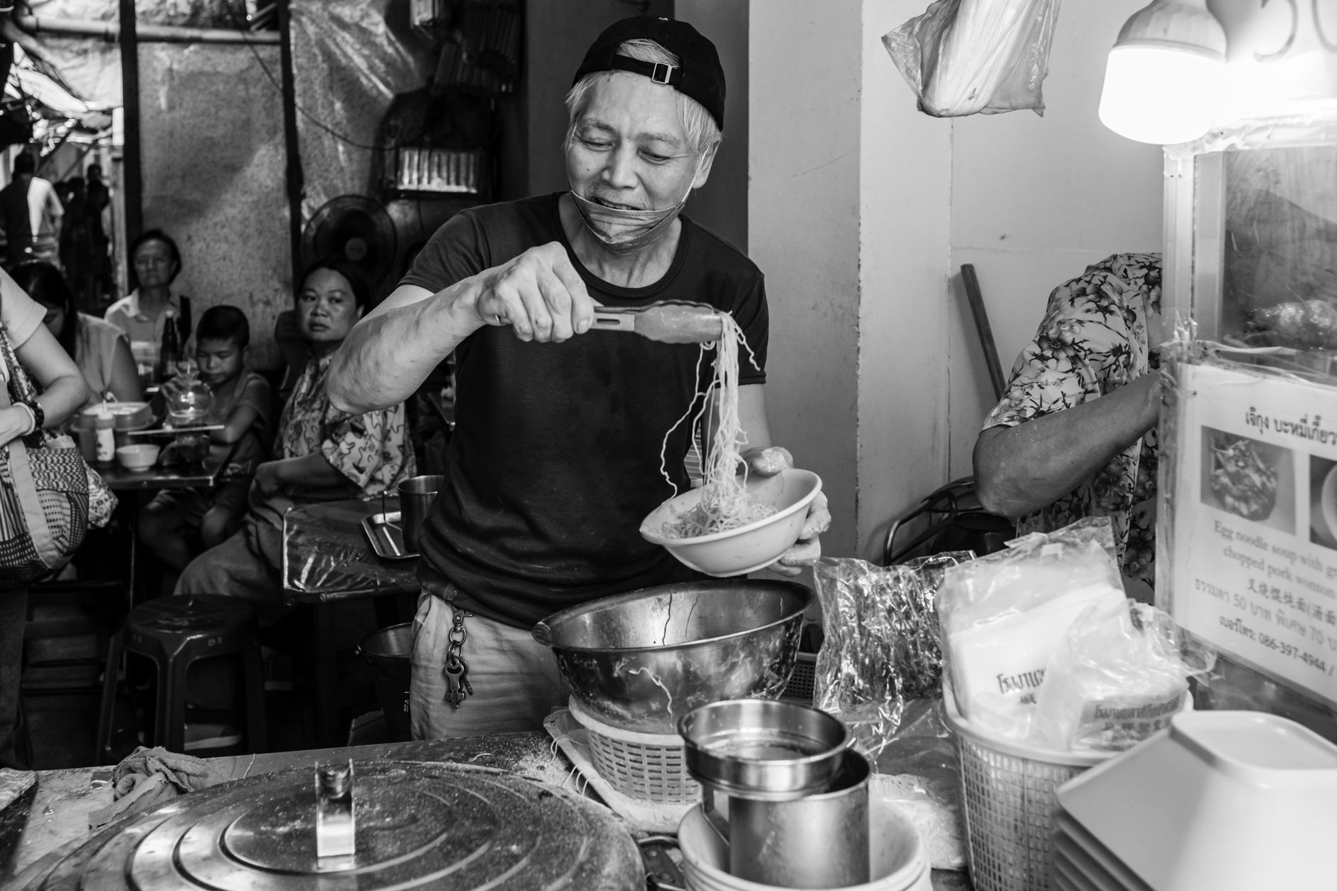 Black and white photo of a street vendor serving noodles, capturing the essence of local market life.