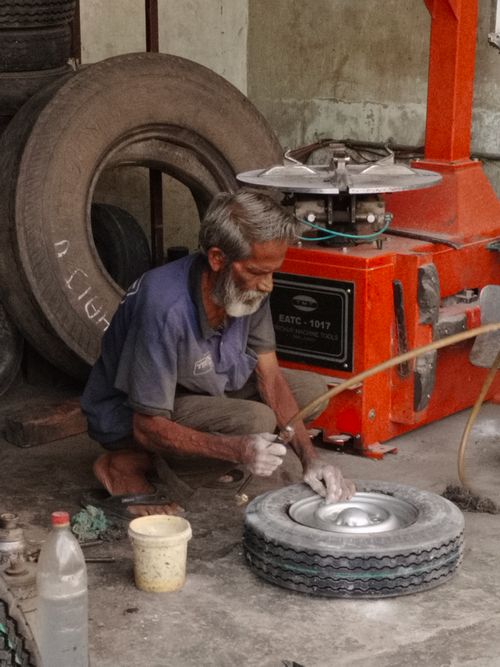 Free An elderly mechanic repairing a tire in a workshop using a machine. Stock Photo