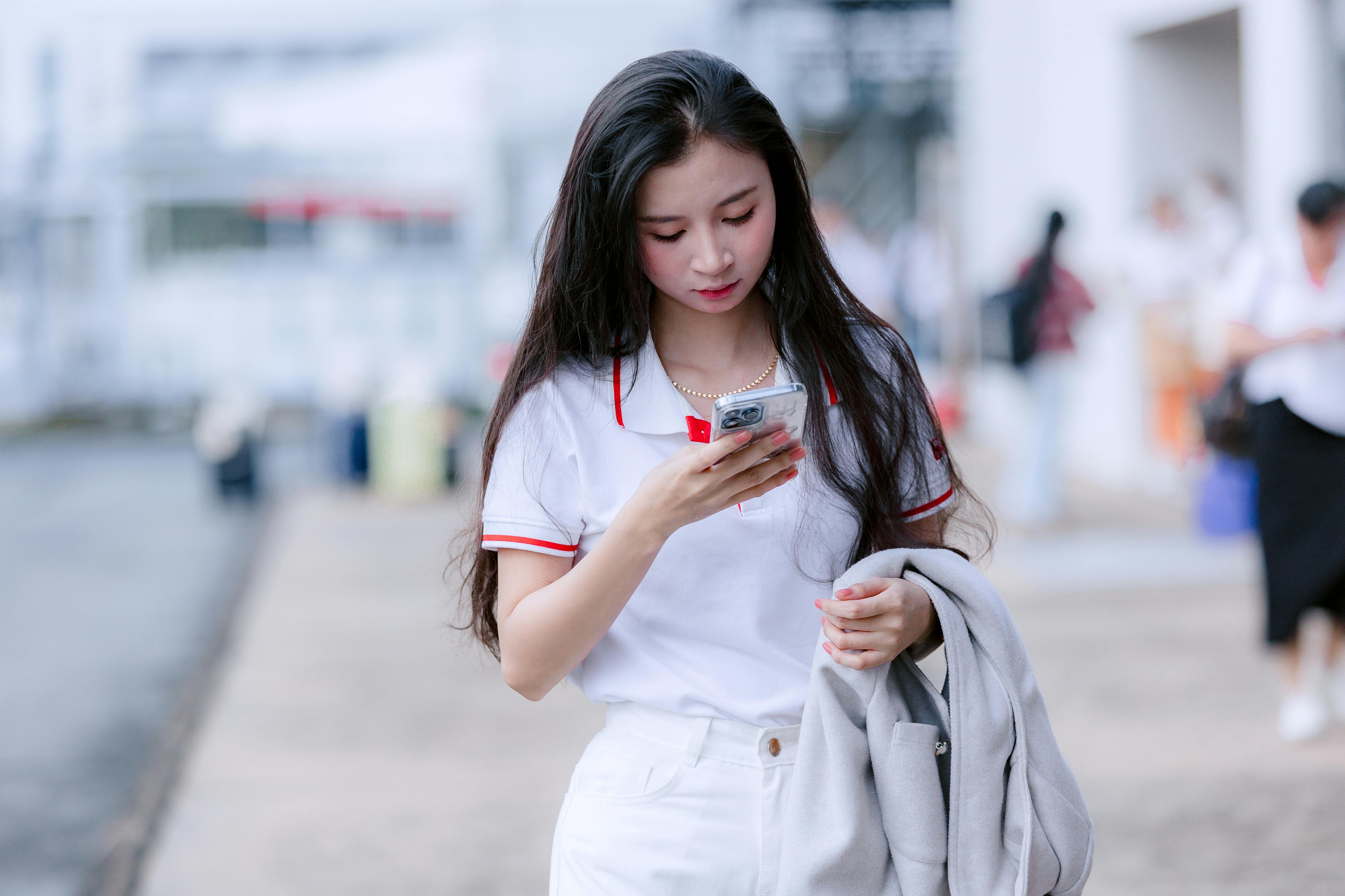 gratis Een jonge vrouw in casual kleding kijkt op haar telefoon terwijl ze buiten loopt. Stockfoto