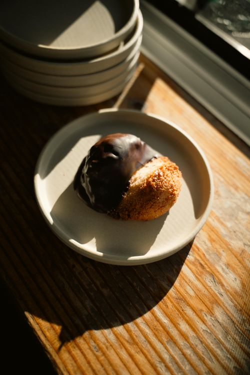 Free A chocolate-dipped coconut pastry in warm natural light on a ceramic plate. Stock Photo