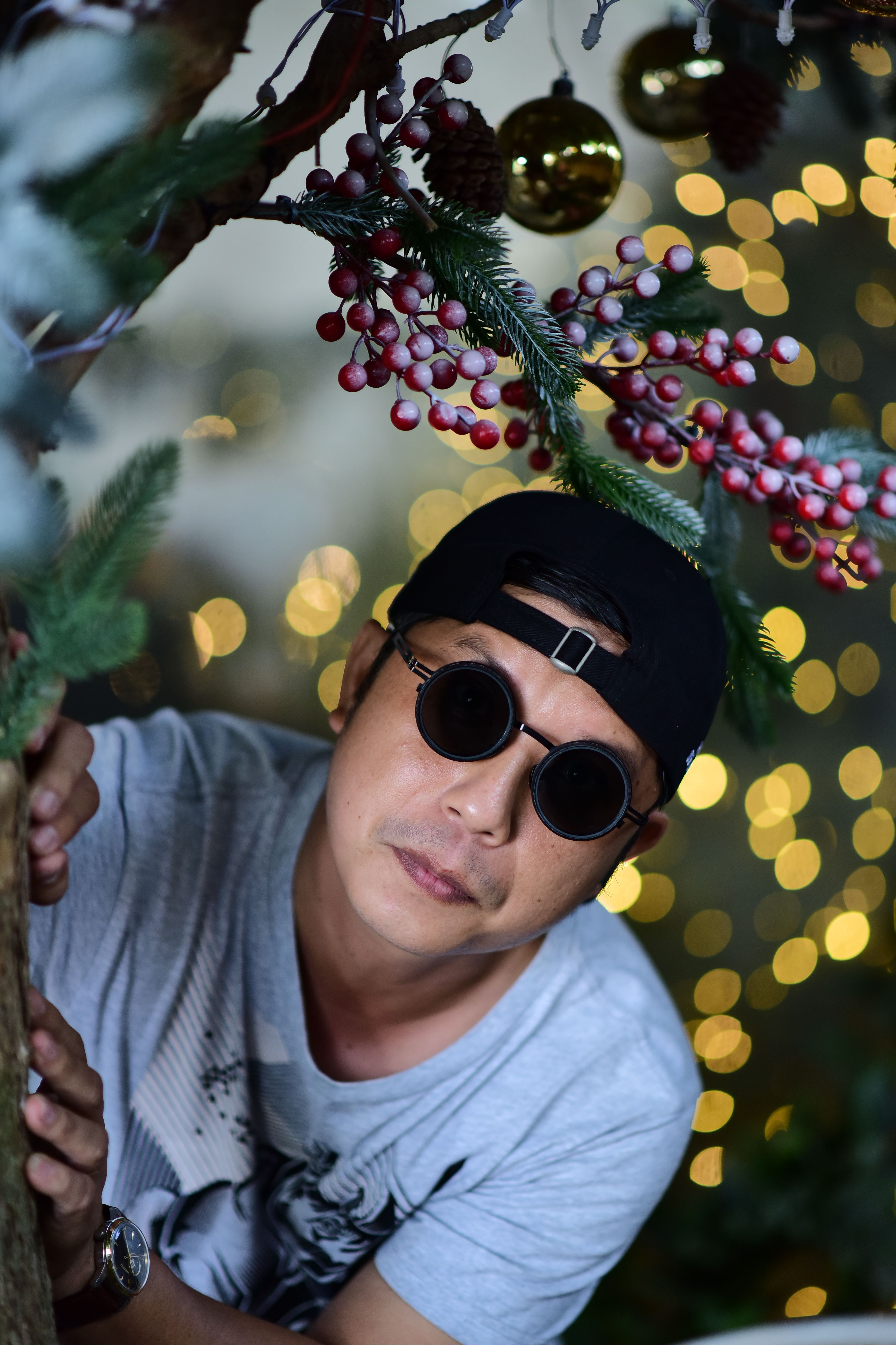 A man in sunglasses peeking from behind festive Christmas decorations with bokeh lights.