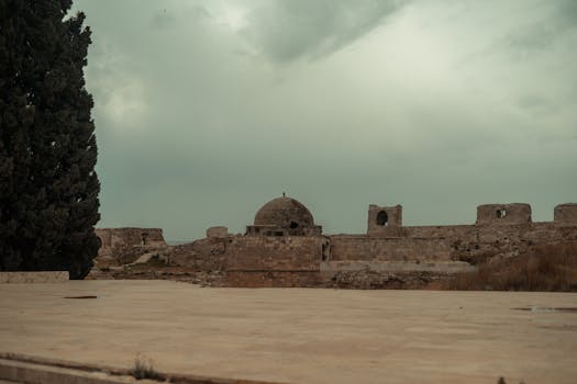 Rooftop view of an ancient citadel in Aleppo, Syria, featuring stone walls and a dome under a cloudy sky.