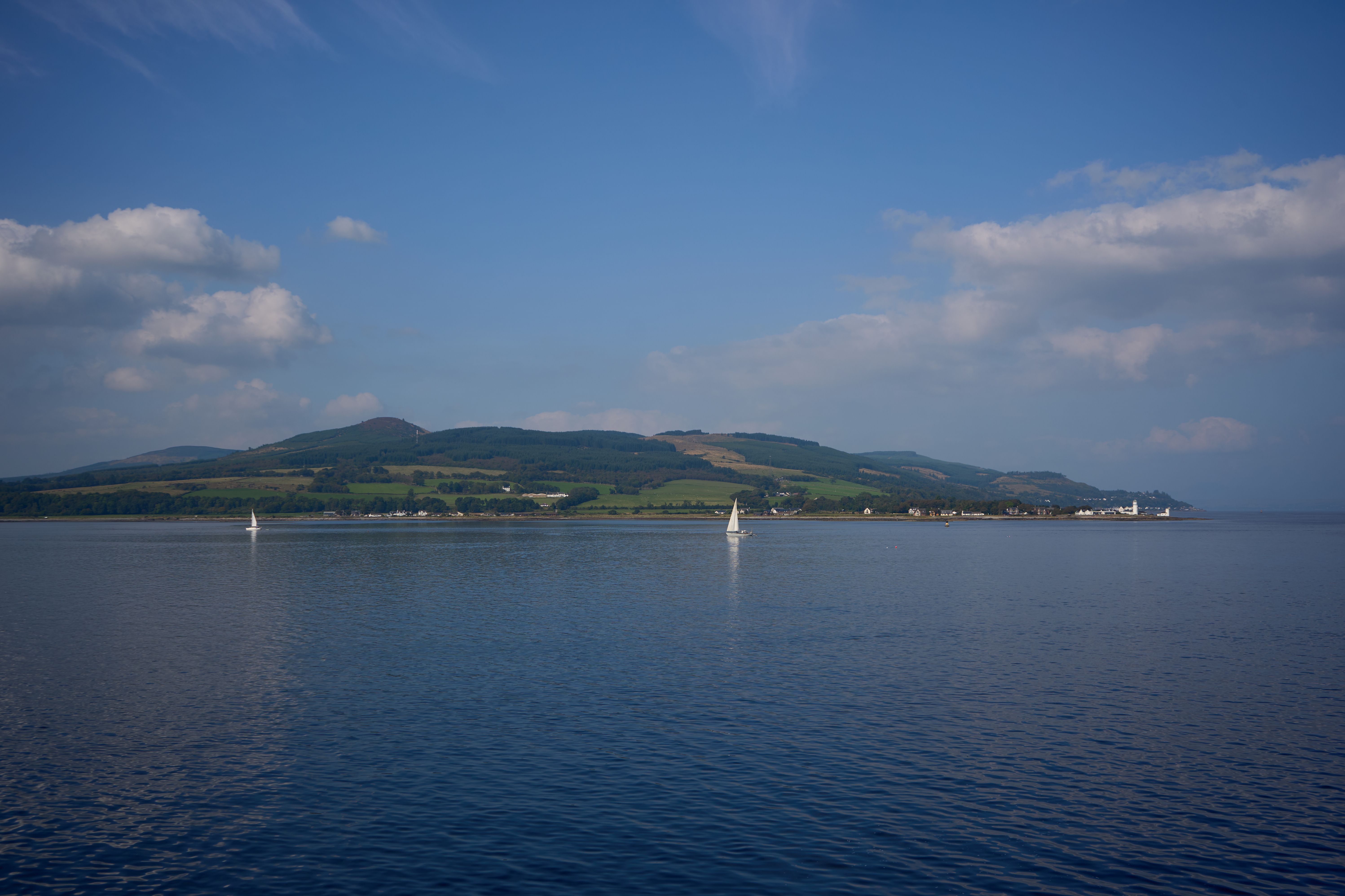 Peaceful summer view of the Isle of Bute, Scotland, with sailboats on calm waters under a blue sky.