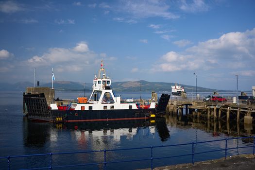 A ferry docked at the Isle of Bute harbor under a sunlit blue sky, Scotland.