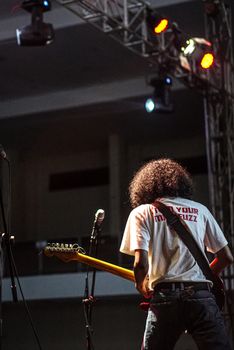 A guitarist performs passionately at a live concert indoors under bright stage lights.