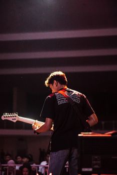 A guitarist playing under a spotlight during a live indoor concert, creating a moody atmosphere.