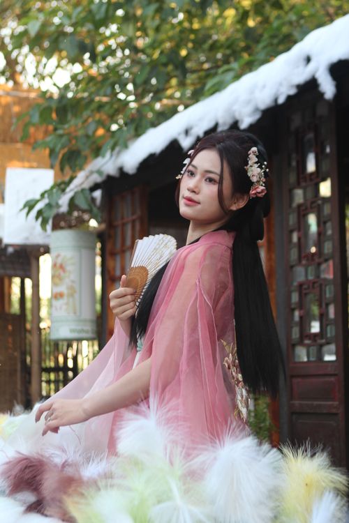 Free Woman dressed in traditional hanfu clothing with floral hairpiece, holding fan outdoors. Stock Photo