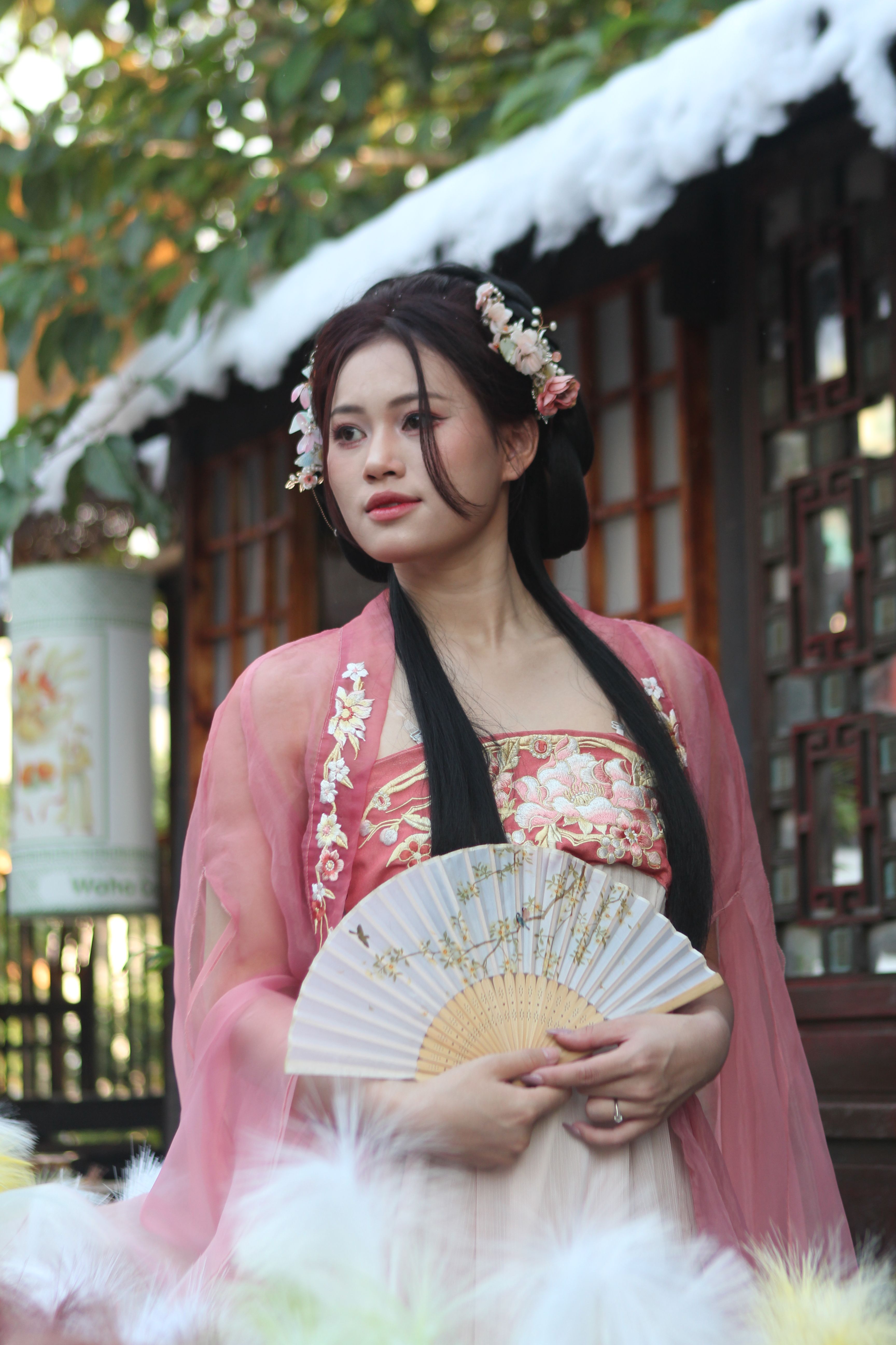 Portrait of a woman in traditional attire with a fan, set in an Oriental garden.