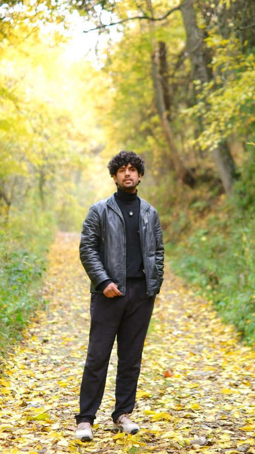 Free A man in a leather jacket stands on a leaf-covered path surrounded by autumn foliage. Stock Photo