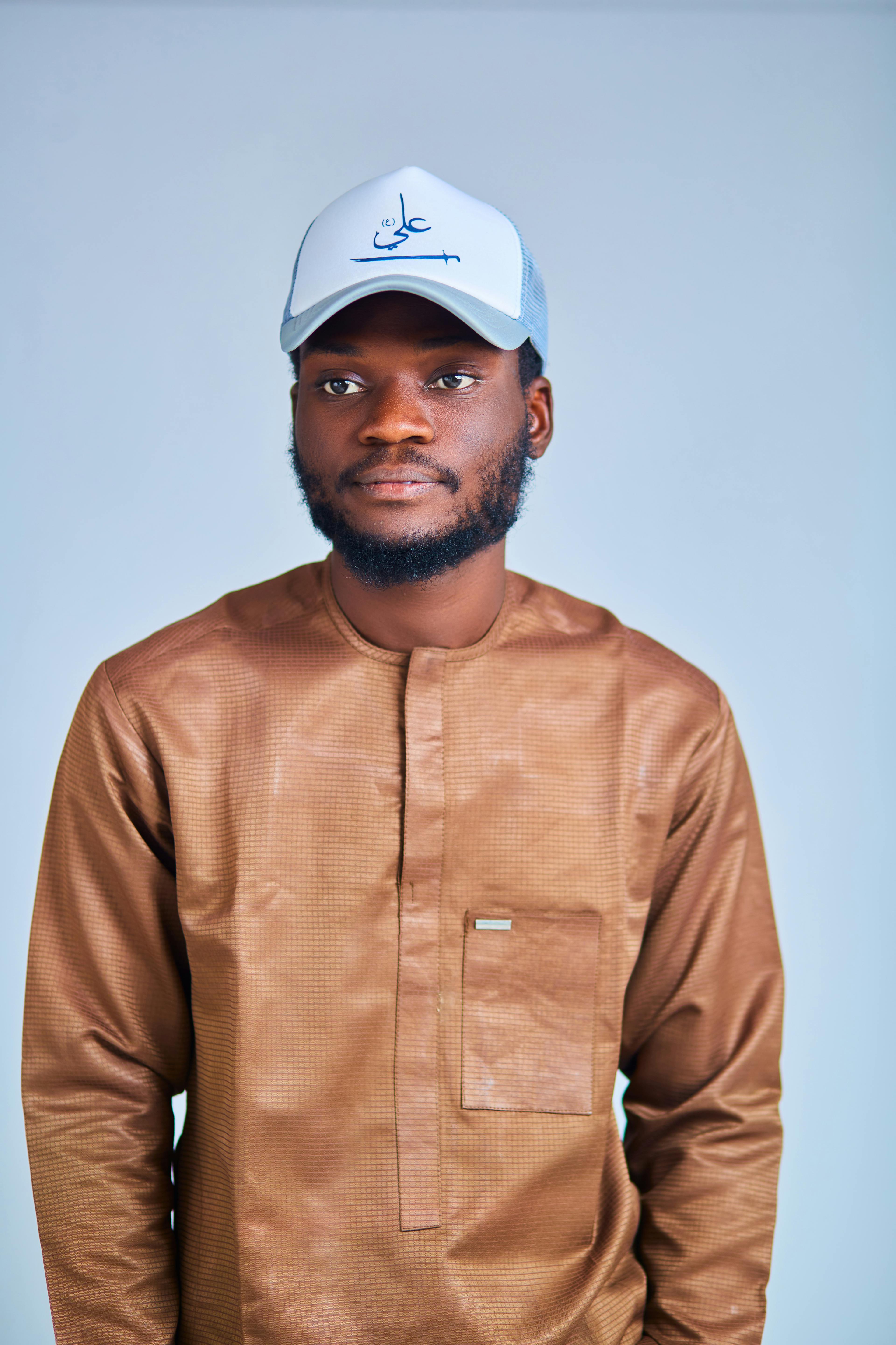 Portrait of a young man wearing traditional brown attire and a cap indoors.