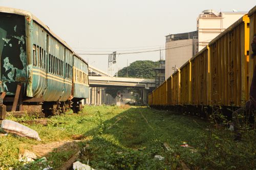 Free Dilapidated train carriages sit on overgrown tracks beside a city railway station. Stock Photo