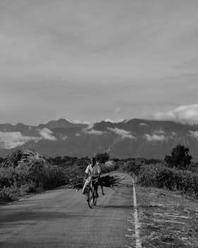 A man cycles on a rural road with hills in the background in Alipurduar, India.
