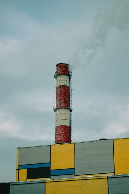 Free Red and white smokestack emitting smoke with colorful industrial building below. Stock Photo