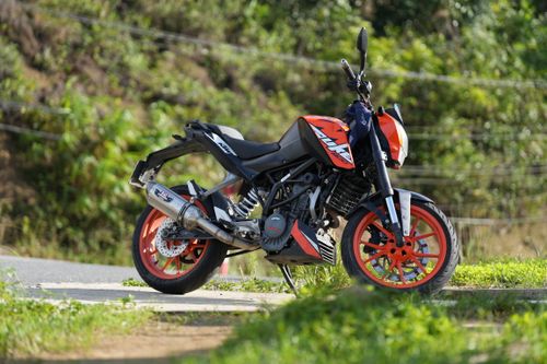 Free Bright orange and black motorcycle parked outdoors on a sunny day with lush greenery. Stock Photo