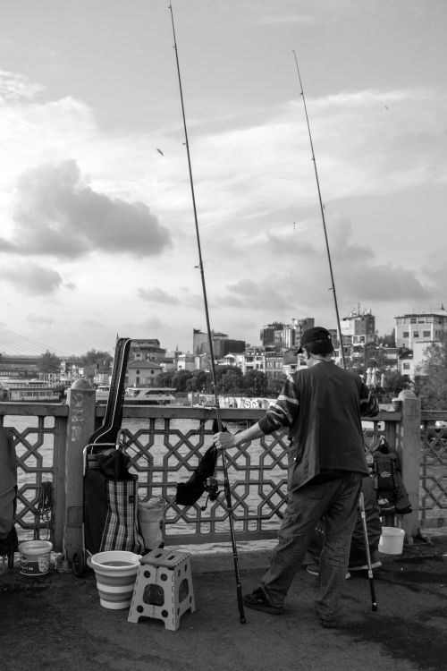 Free Man fishing on a bridge with city skyline in the background, captured in black and white. Stock Photo