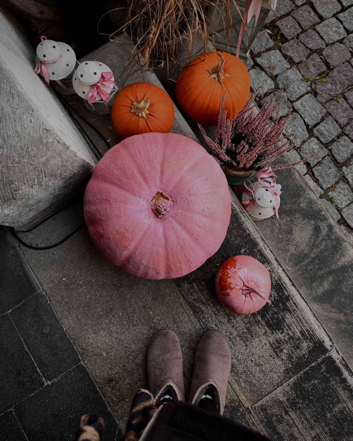 A vibrant autumn scene with pink and orange pumpkins next to decorative candles and boots on a cobblestone path. Stock Photo.