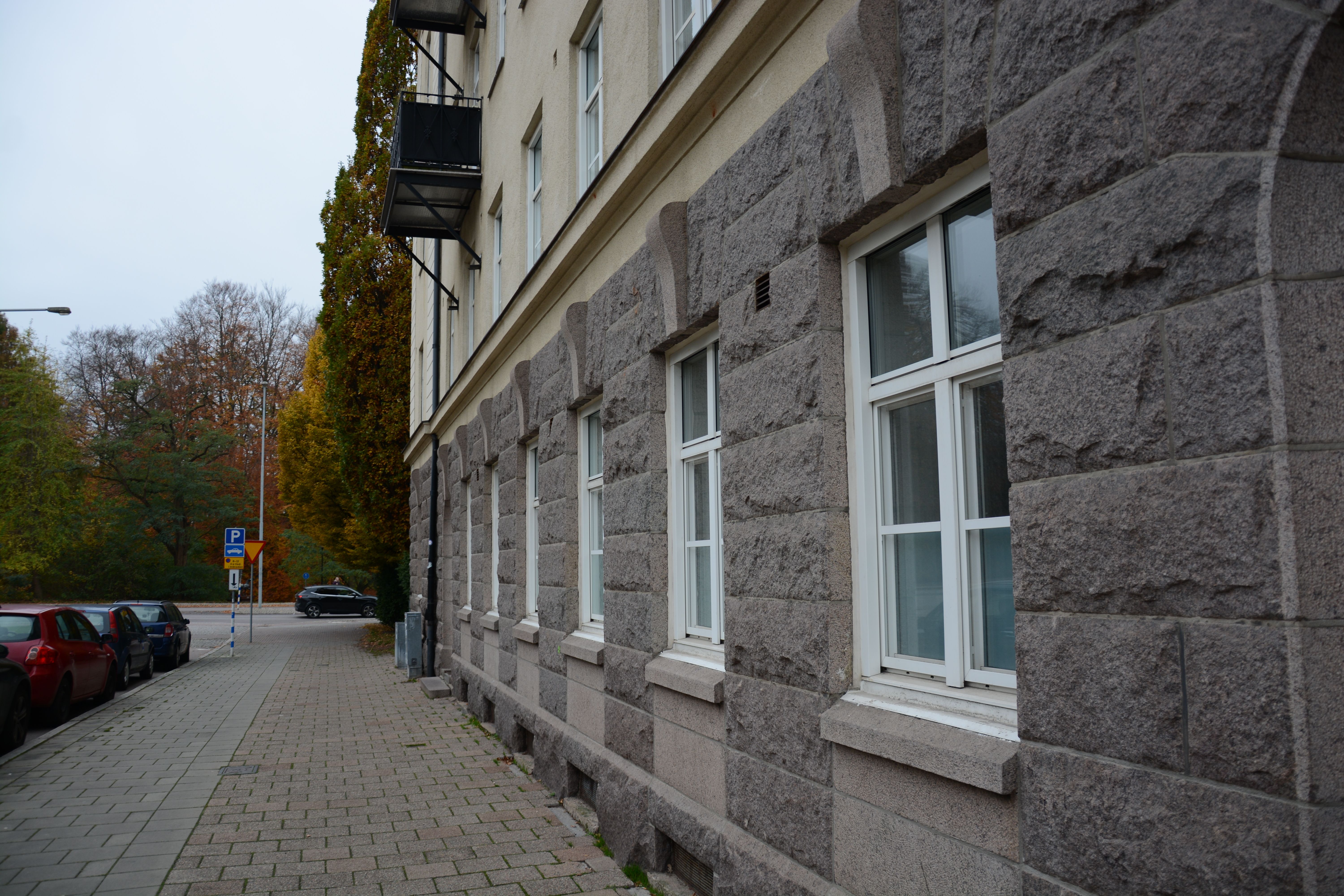 Exterior view of a historic stone building with autumn trees on a city sidewalk.