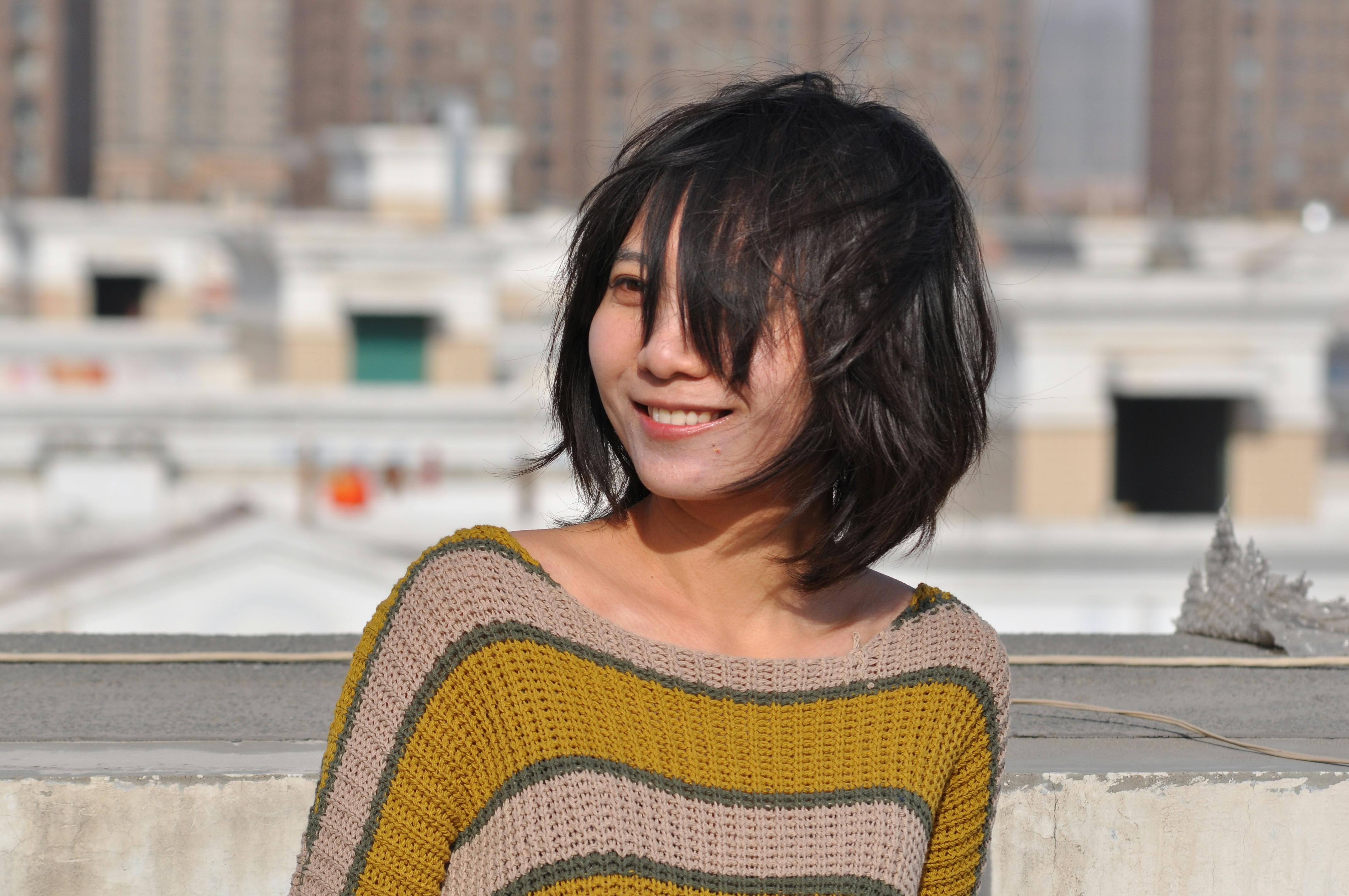 A candid photo of a smiling woman with wind-blown hair on a rooftop.