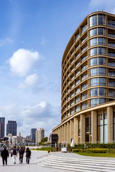 Contemporary building by river with people walking, showcasing modern architecture and cityscape.