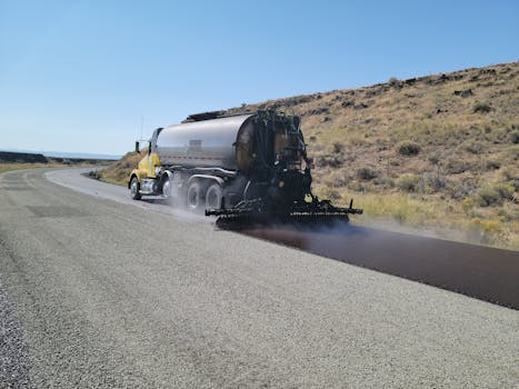 A road tanker applying asphalt on a rural road in Oregon under clear skies.