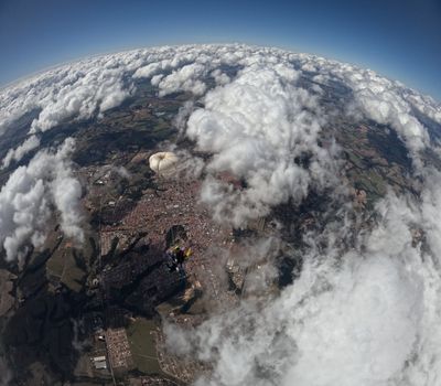 Skydiver with parachute above city and clouds, aerial perspective.