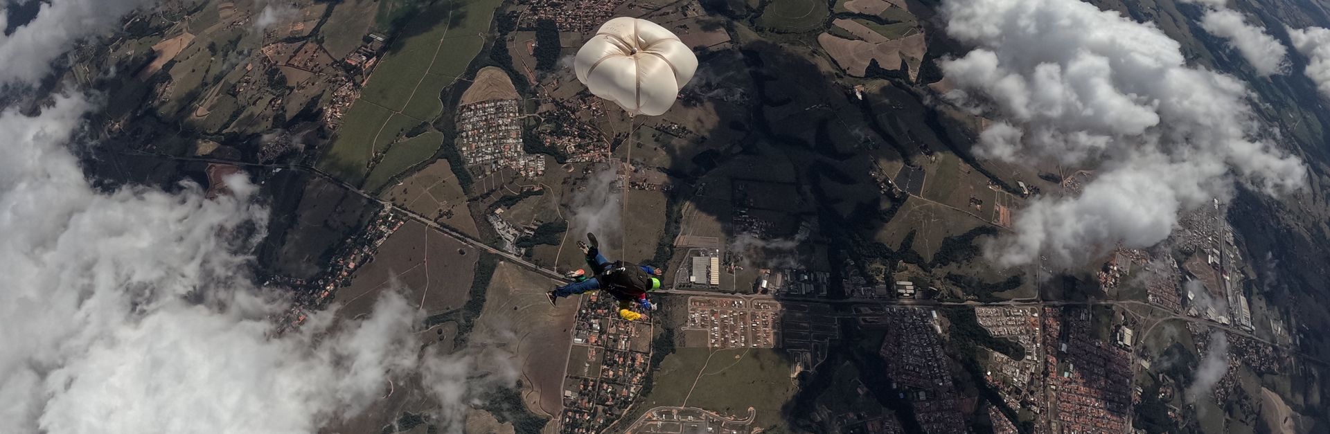 Aerial view of a skydiver with parachute above picturesque terrain and clouds.