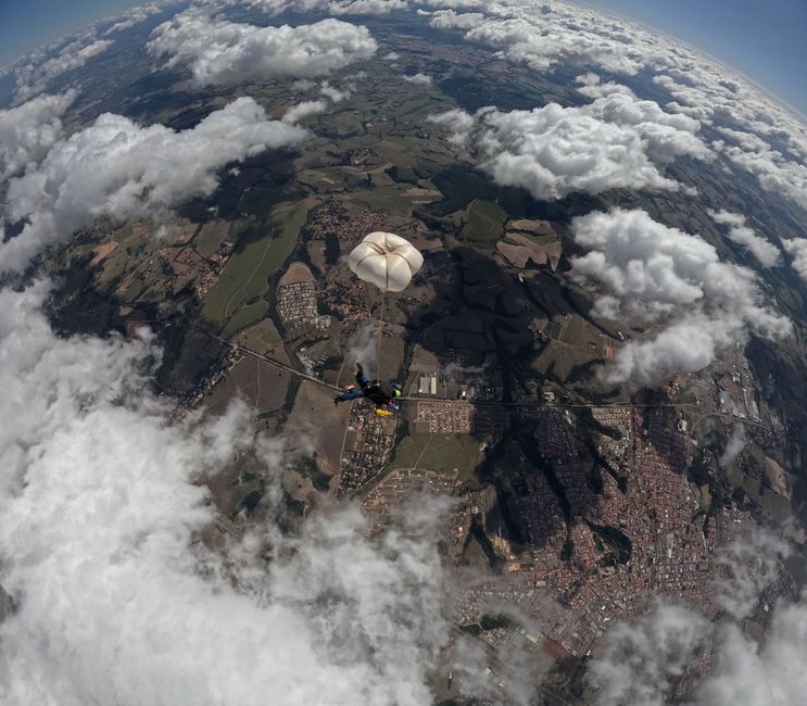 Vista aérea de um paraquedista com paraquedas sobre uma paisagem pitoresca e nuvens.
