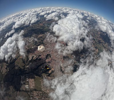 A skydiver floats with a parachute above a sprawling urban landscape beneath clouds.