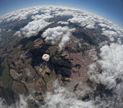 Breathtaking aerial photo of a parachutist above a city's landscape among clouds.