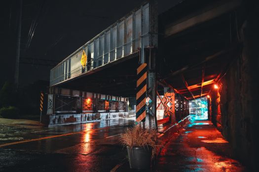 Dimly lit urban underpass at night with rain-soaked reflections and vibrant lighting.