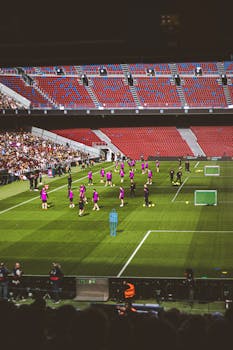 Soccer team players warming up in a large stadium with a crowd watching.