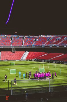 Soccer team practicing on a green field in a large empty stadium, preparing for a match.
