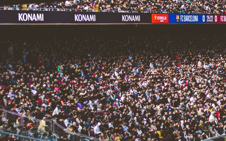 A large crowd enjoys a live football match in a packed stadium under a clear sky.