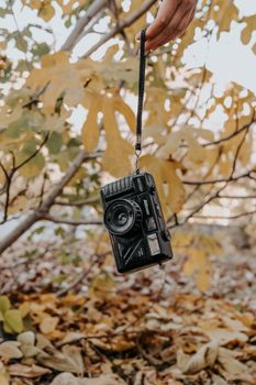 Old film camera hanging from a hand, surrounded by fall leaves.