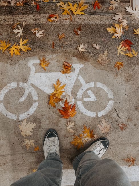 Feet in sneakers stand on fall leaves over a bicycle lane symbol.