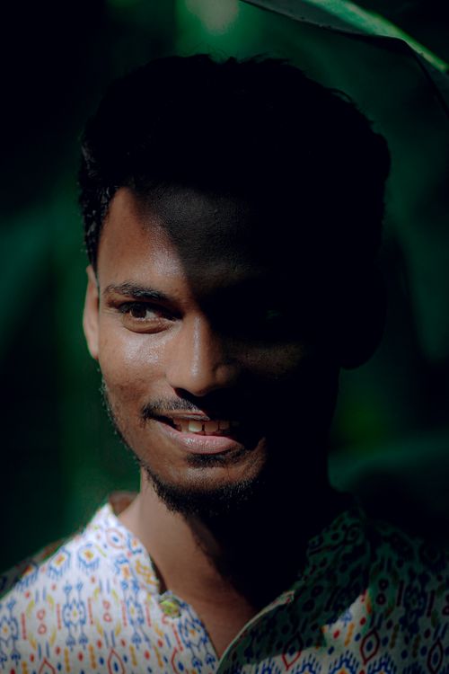 Free Close-up portrait of a smiling man with dappled sunlight on his face, surrounded by foliage. Stock Photo