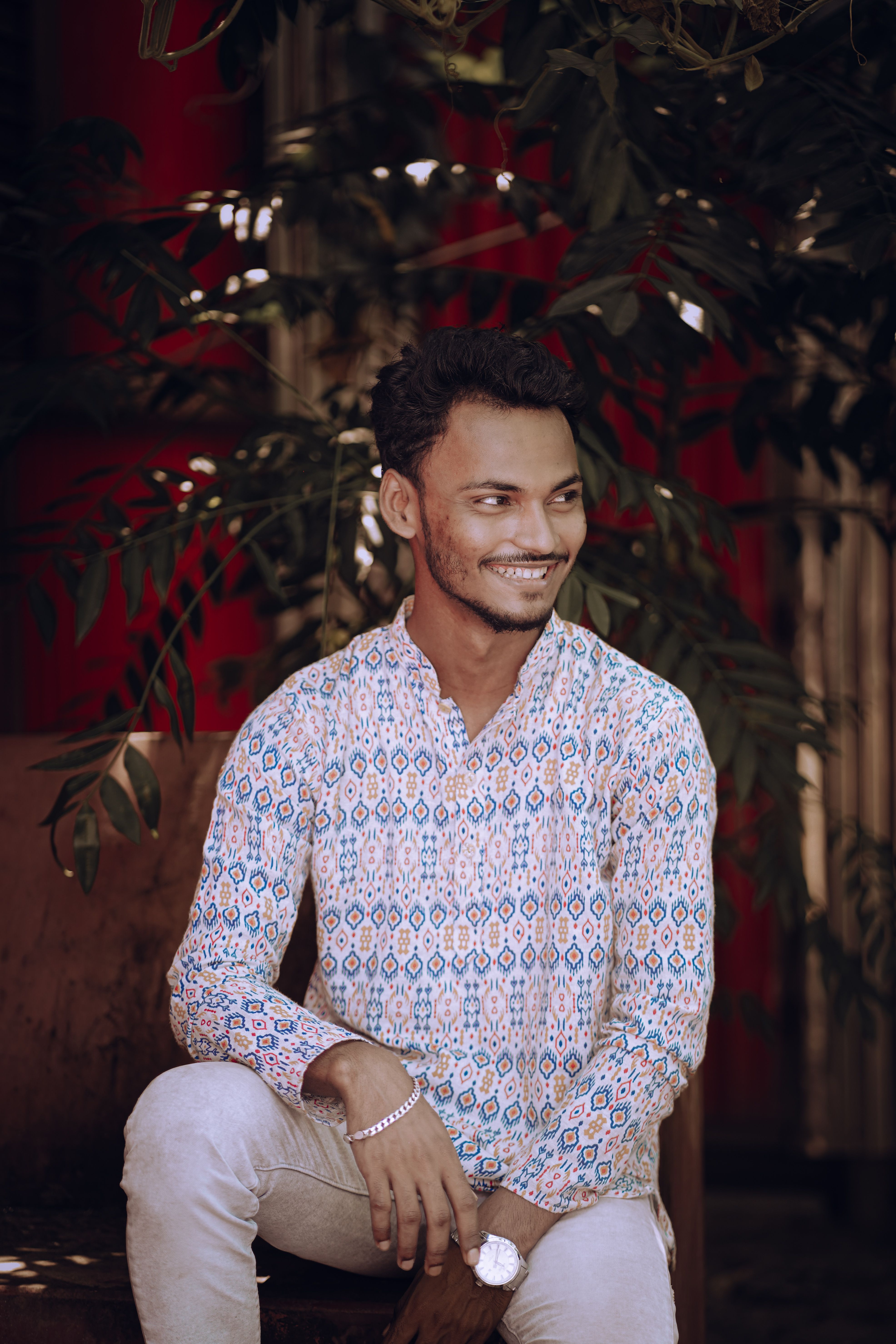 Portrait of a young man in a casual printed shirt sitting and smiling outdoors, exuding a warm and relaxed vibe.