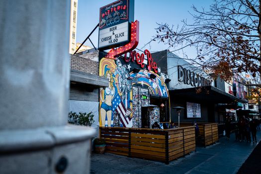 Street view of a vibrant pizza restaurant with neon lights and mural art in the evening.