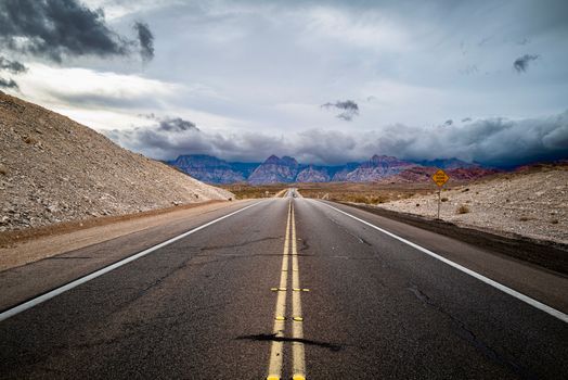 A deserted highway in a barren landscape with mountains under a dramatic sky.