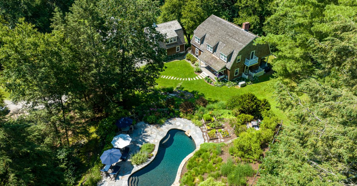 Aerial view of a charming house with a swimming pool surrounded by lush greenery in a serene setting.