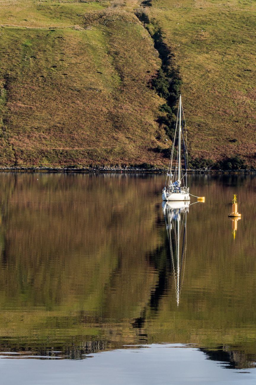 A tranquil scene of a yacht reflecting on calm waters amidst Scotland's stunning landscape.